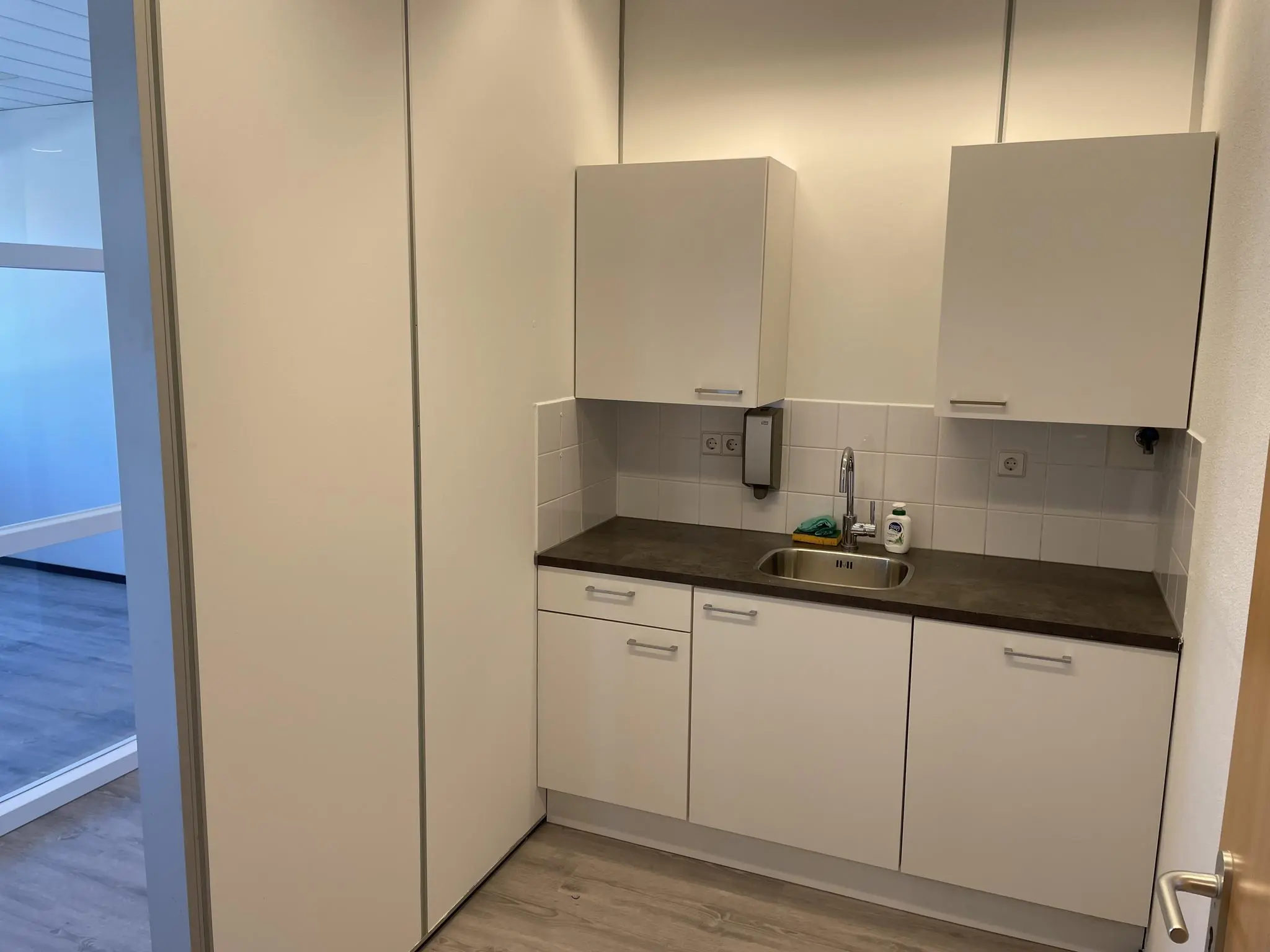 Kleine, moderne kitchenette met witte kasten en een donker werkblad in een kantoor aan de Laan van s-Gravenmade.